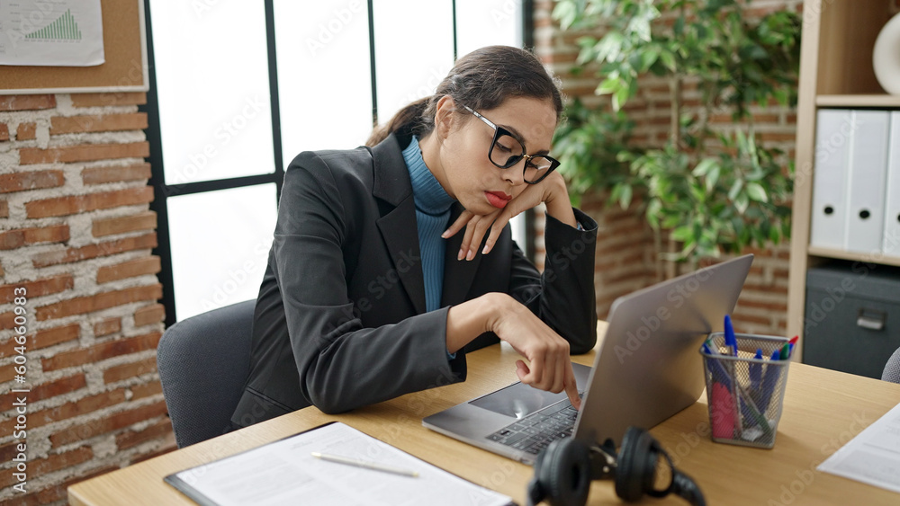 Young beautiful hispanic woman business worker using laptop with boring expression at office Young beautiful hispanic woman business worker using laptop with boring expression at office