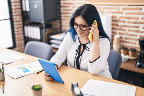 Young caucasian woman business worker using touchpad talking on smartphone at office