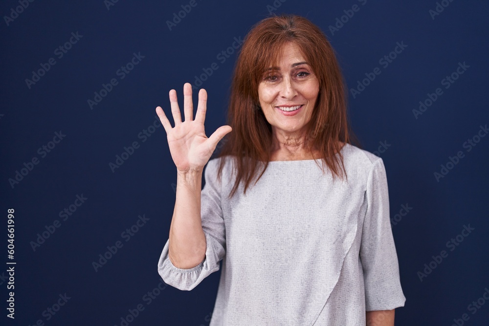 Middle age woman standing over blue background showing and pointing up with fingers number five while smiling confident and happy. Middle age woman standing over blue background showing and pointing up with fingers number five while smiling confident and happy.