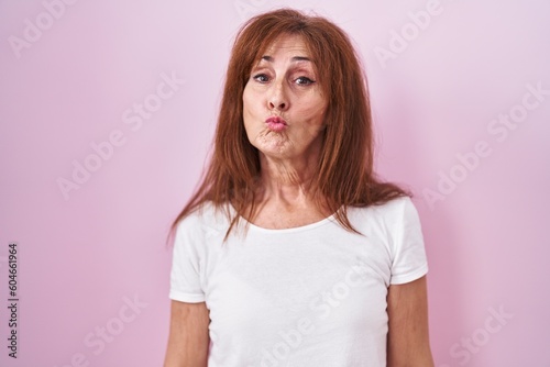 Middle age woman standing over pink background looking at the camera blowing a kiss on air being lovely and sexy. love expression.