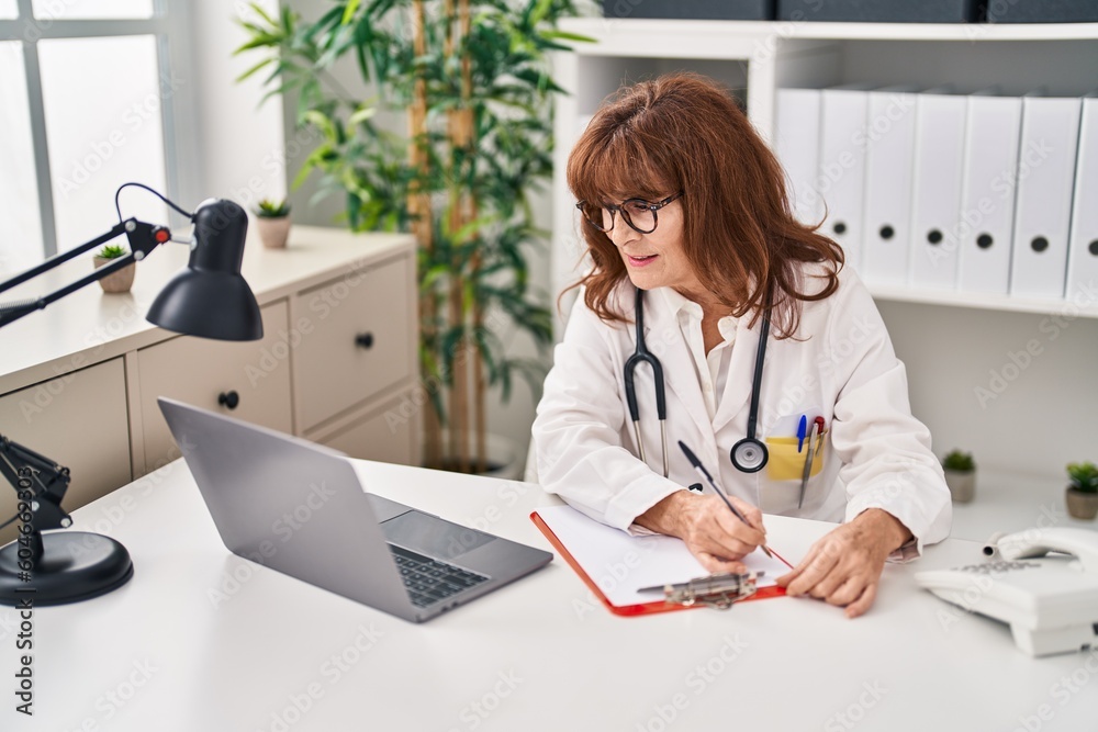 Middle age woman wearing doctor uniform writing on paperwork at clinic Middle age woman wearing doctor uniform writing on paperwork at clinic