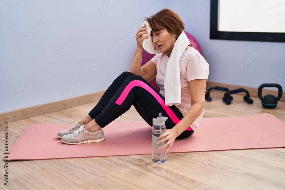 Middle age woman using towel sitting on yoga mat at sport center