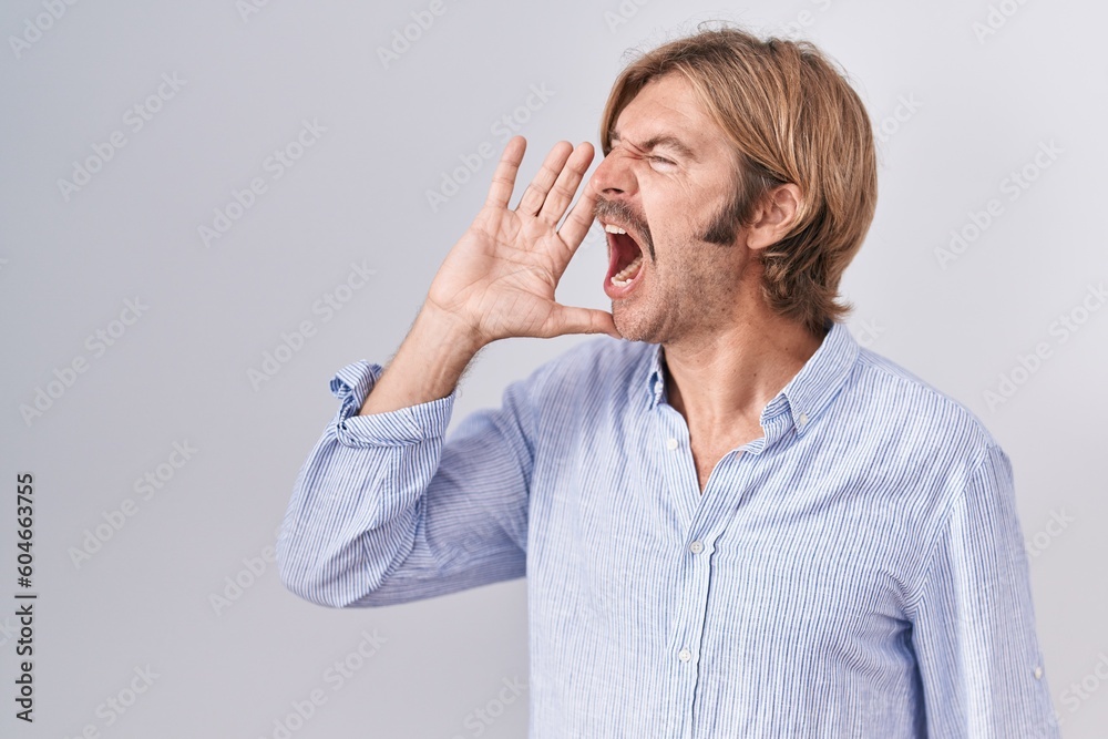 Caucasian man with mustache standing over white background shouting and screaming loud to side with hand on mouth. communication concept. Caucasian man with mustache standing over white background shouting and screaming loud to side with hand on mouth. communication concept.