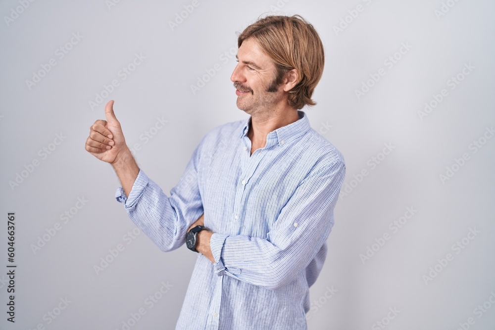 Caucasian man with mustache standing over white background looking proud, smiling doing thumbs up gesture to the side Caucasian man with mustache standing over white background looking proud, smiling doing thumbs up gesture to the side