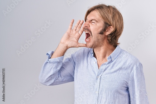Caucasian man with mustache standing over white background shouting and screaming loud to side with hand on mouth. communication concept.
