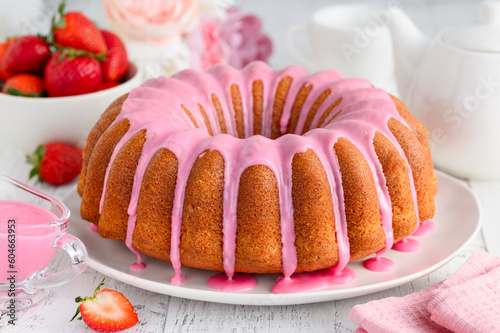 Strawberry bundt cake with pink icing on a plate. Summer berry pastry. White wooden background. Selective focus