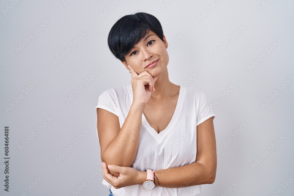Young asian woman with short hair standing over isolated background with hand on chin thinking about question, pensive expression. smiling with thoughtful face. doubt concept. Young asian woman with short hair standing over isolated background with hand on chin thinking about question, pensive expression. smiling with thoughtful face. doubt concept.