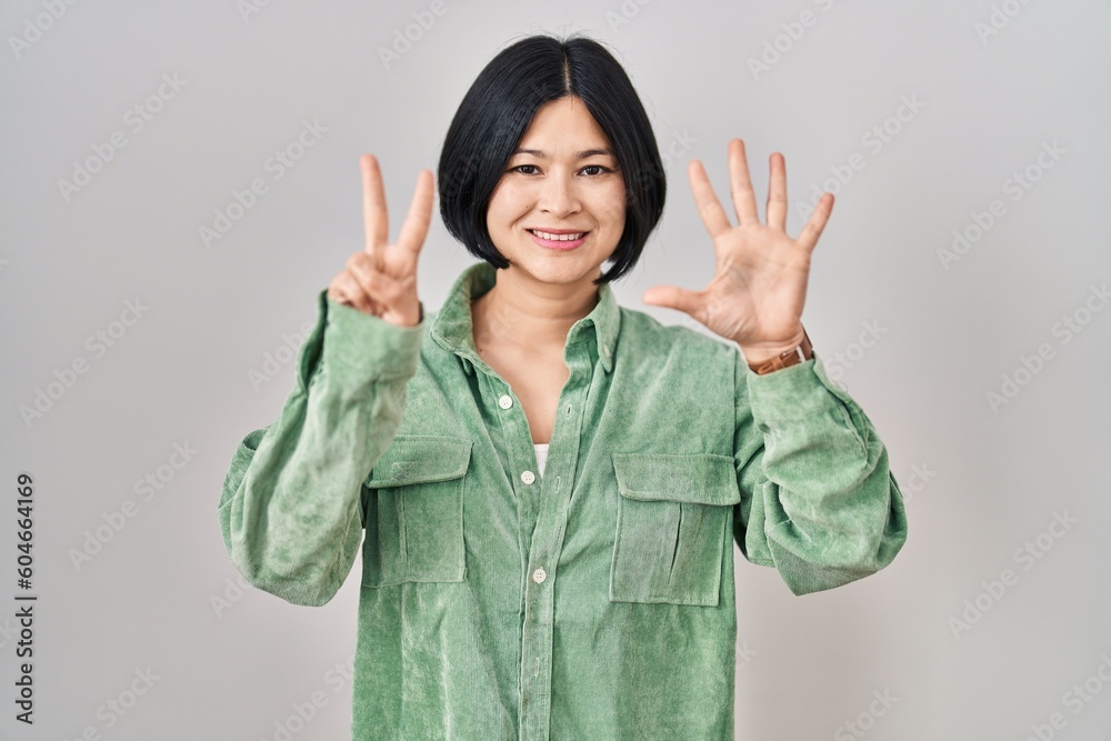 Young asian woman standing over white background showing and pointing up with fingers number seven while smiling confident and happy. Young asian woman standing over white background showing and pointing up with fingers number seven while smiling confident and happy.