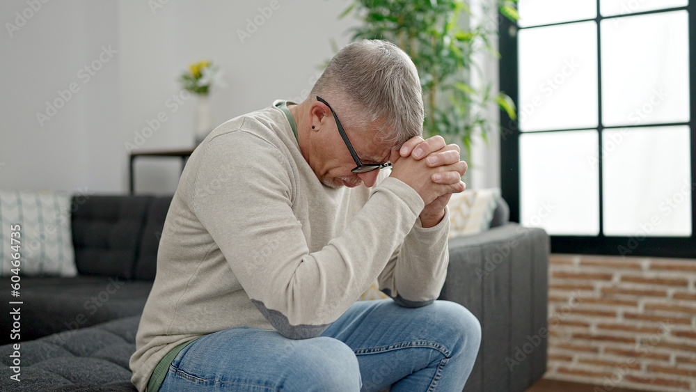 Middle age grey-haired man stressed sitting on sofa at home Middle age grey-haired man stressed sitting on sofa at home