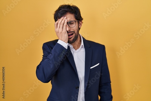 Handsome latin man standing over yellow background yawning tired covering half face, eye and mouth with hand. face hurts in pain. © Krakenimages.com