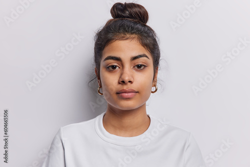 Canvas Print Portrait of beautiful serious brunette woman focused at camera has dark hair combed in bun dressed in casual t shirt isolated over white background