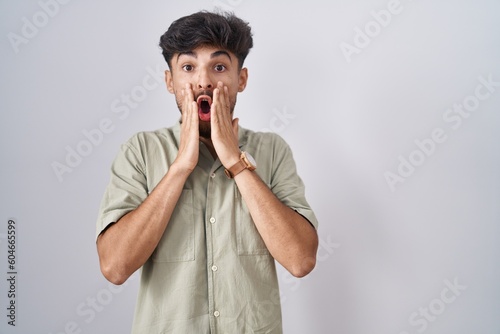 Arab man with beard standing over white background afraid and shocked  surprise and amazed expression with hands on face
