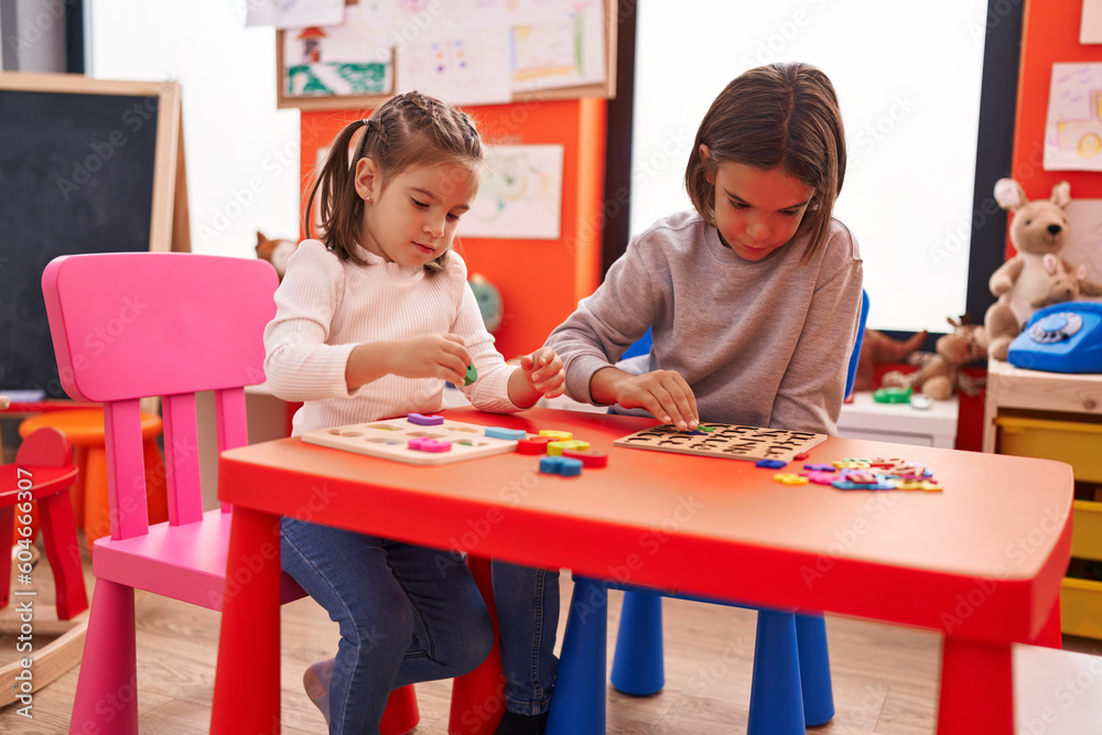Adorable boy and girl playing with maths puzzle game sitting on table at kindergarten Adorable boy and girl playing with maths puzzle game sitting on table at kindergarten