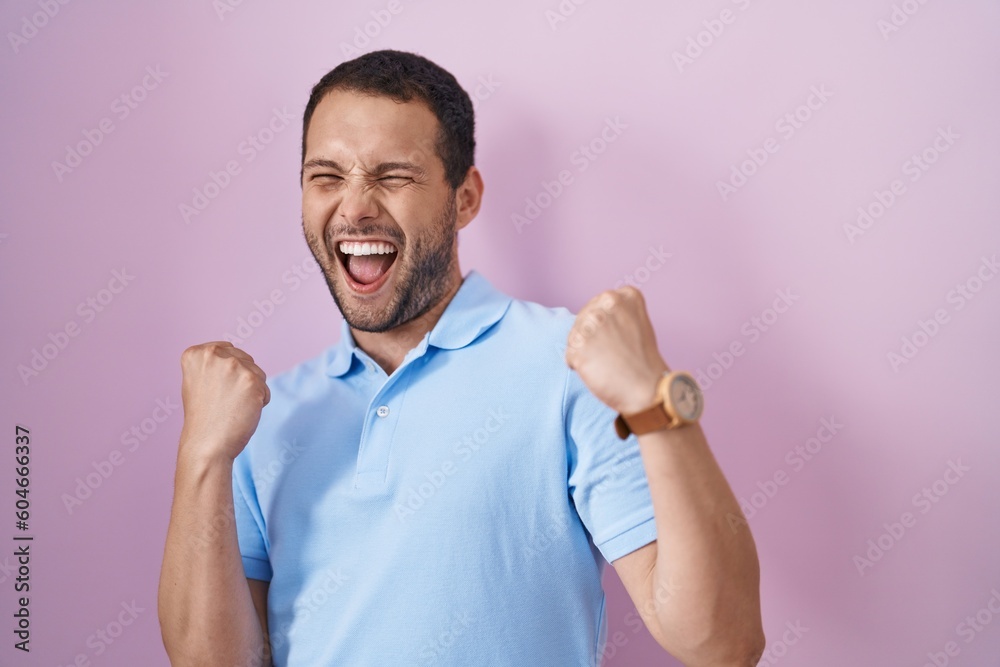 Hispanic man standing over pink background very happy and excited doing winner gesture with arms raised, smiling and screaming for success. celebration concept. Hispanic man standing over pink background very happy and excited doing winner gesture with arms raised, smiling and screaming for success. celebration concept.
