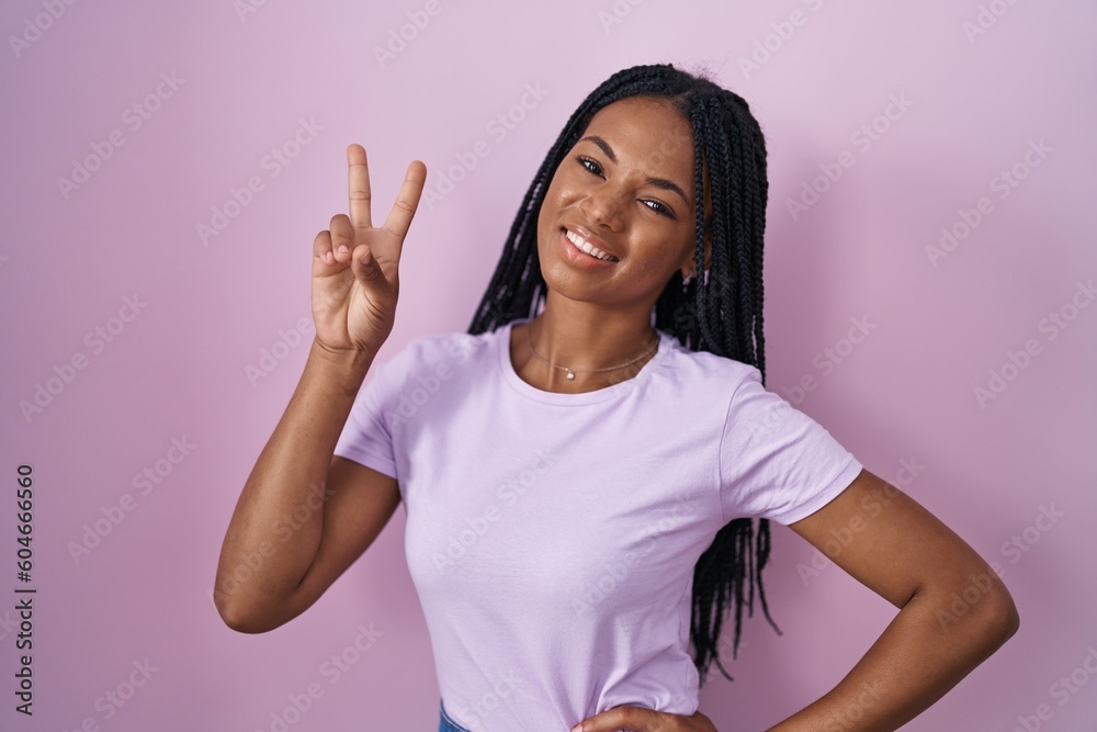 African american woman with braids standing over pink background smiling looking to the camera showing fingers doing victory sign. number two. African american woman with braids standing over pink background smiling looking to the camera showing fingers doing victory sign. number two.