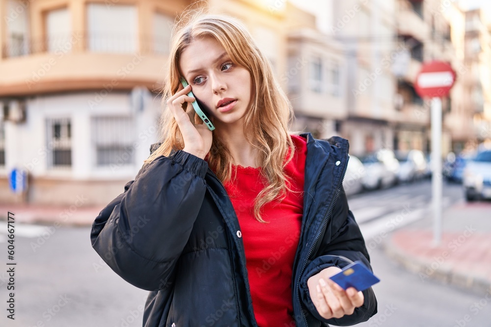 Young blonde woman talking on smartphone holding credit card at street Young blonde woman talking on smartphone holding credit card at street