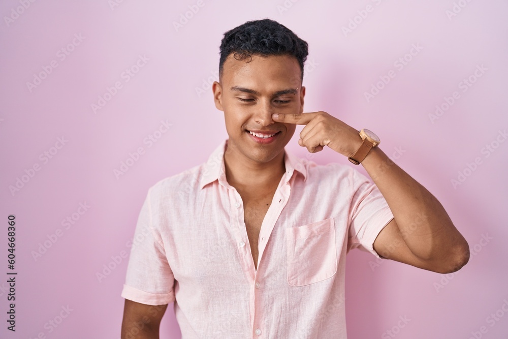 Young hispanic man standing over pink background pointing with hand finger to face and nose, smiling cheerful. beauty concept Young hispanic man standing over pink background pointing with hand finger to face and nose, smiling cheerful. beauty concept