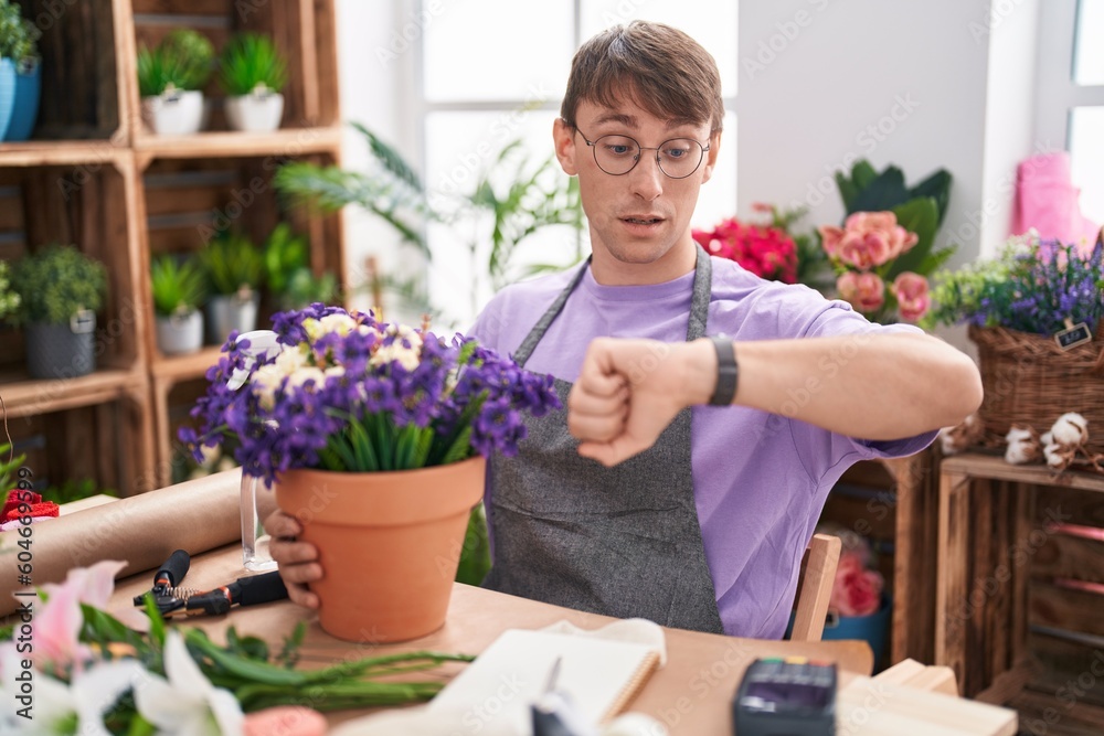 Caucasian blond man working at florist shop looking at the watch time worried, afraid of getting late