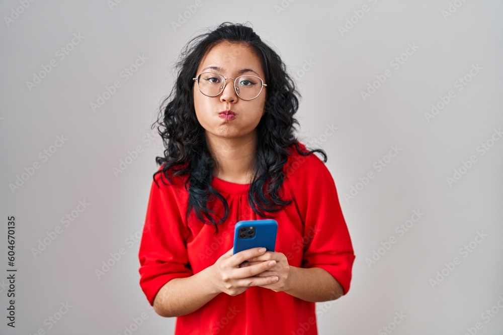 Young asian woman using smartphone typing message puffing cheeks with funny face. mouth inflated with air, catching air. Young asian woman using smartphone typing message puffing cheeks with funny face. mouth inflated with air, catching air.