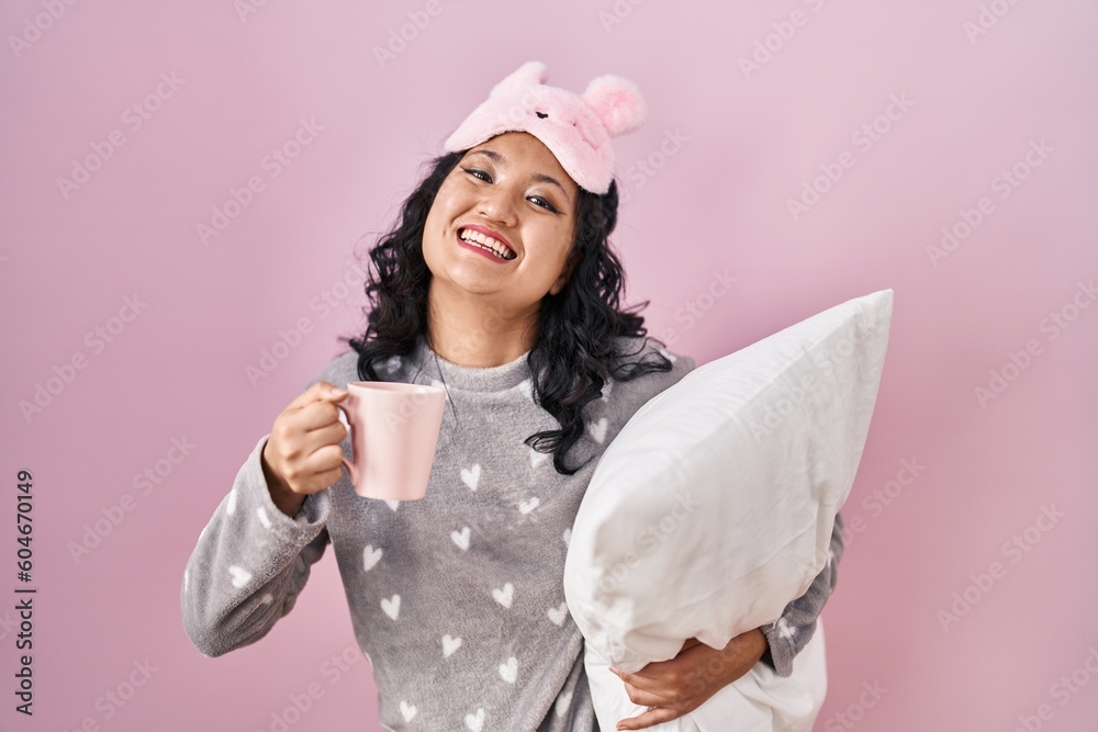 Young asian woman wearing sleep mask and pajama hugging pillow drinking coffee celebrating crazy and amazed for success with open eyes screaming excited. Young asian woman wearing sleep mask and pajama hugging pillow drinking coffee celebrating crazy and amazed for success with open eyes screaming excited.