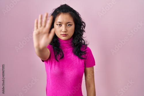 Young asian woman standing over pink background doing stop sing with palm of the hand. warning expression with negative and serious gesture on the face.