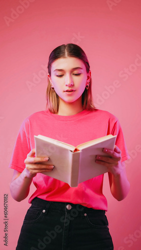 Book reading. Learning student. Concentrated involved in interesting plot girl novel in one breath isolated on neon color pink background. © golubovy