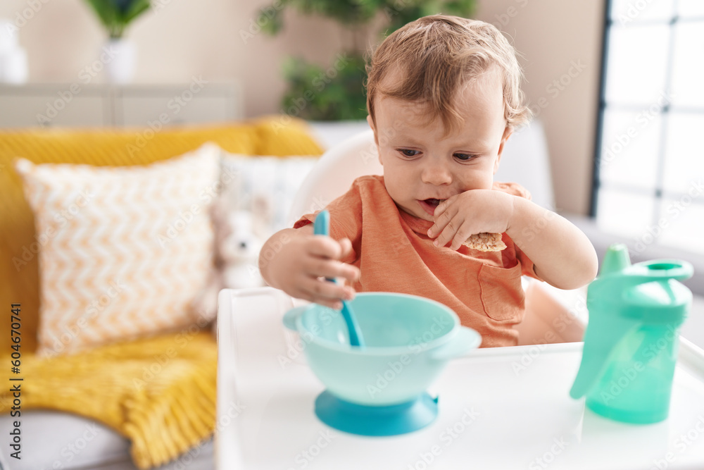 Adorable blond toddler sitting on highchair eating snack at home Adorable blond toddler sitting on highchair eating snack at home