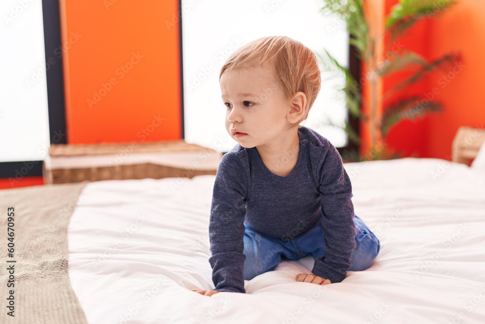 Fototapeta premium Adorable blond toddler sitting on bed with with relaxed expression at bedroom