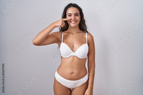 Young hispanic woman wearing white lingerie pointing with hand finger to face and nose, smiling cheerful. beauty concept © Krakenimages.com