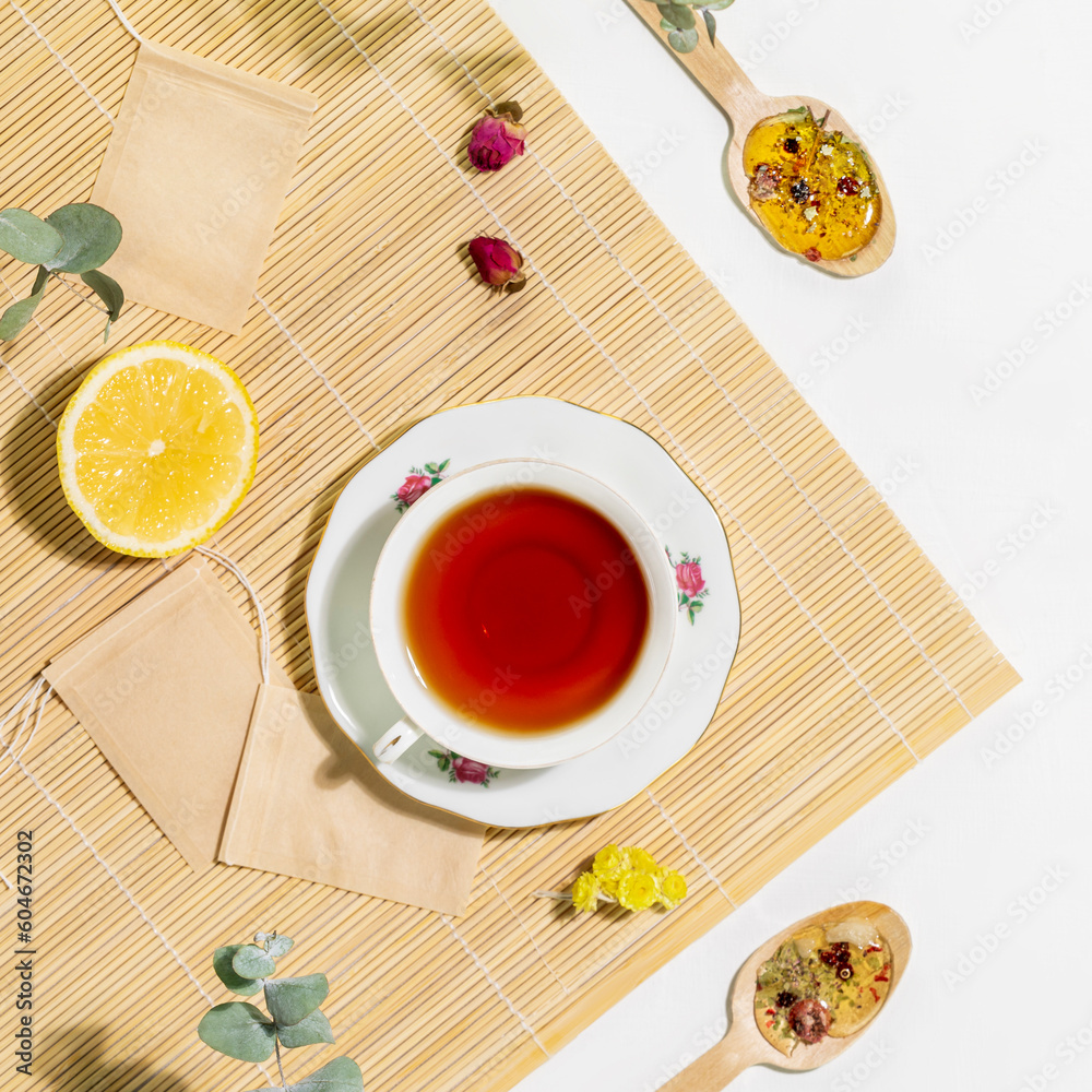 Tea time. Healing natural herbal tea. Sustainable morning composition with cup of herbal tea with spoons, slice of lemon and dry flowers on wooden napkin on white background. Flat lay