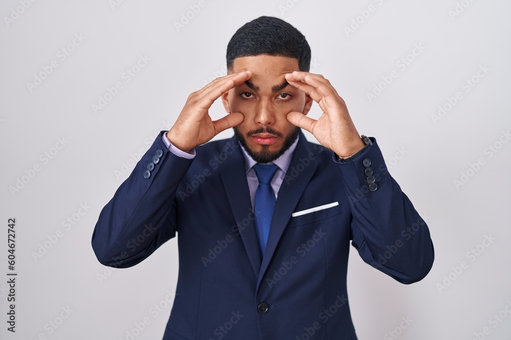 Young hispanic man wearing business suit and tie trying to open eyes with fingers, sleepy and tired for morning fatigue Young hispanic man wearing business suit and tie trying to open eyes with fingers, sleepy and tired for morning fatigue