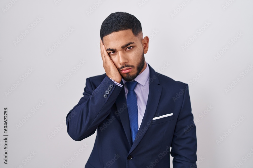 Young hispanic man wearing business suit and tie thinking looking tired and bored with depression problems with crossed arms. Young hispanic man wearing business suit and tie thinking looking tired and bored with depression problems with crossed arms.