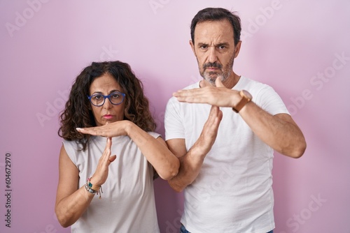 Middle age hispanic couple together over pink background doing time out gesture with hands, frustrated and serious face