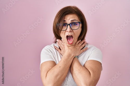 Middle age hispanic woman standing over pink background shouting suffocate because painful strangle. health problem. asphyxiate and suicide concept.