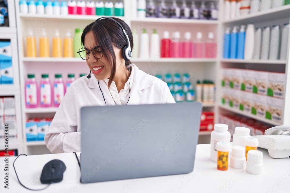 Young arab woman working at pharmacy drugstore using laptop with hand on stomach because nausea, painful disease feeling unwell. ache concept.