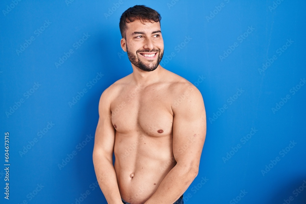 Fototapeta premium Handsome hispanic man standing shirtless looking away to side with smile on face, natural expression. laughing confident.