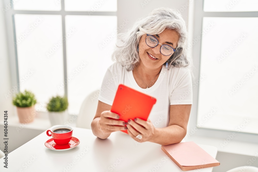 Middle age woman using touchpad sitting on table at home Middle age woman using touchpad sitting on table at home