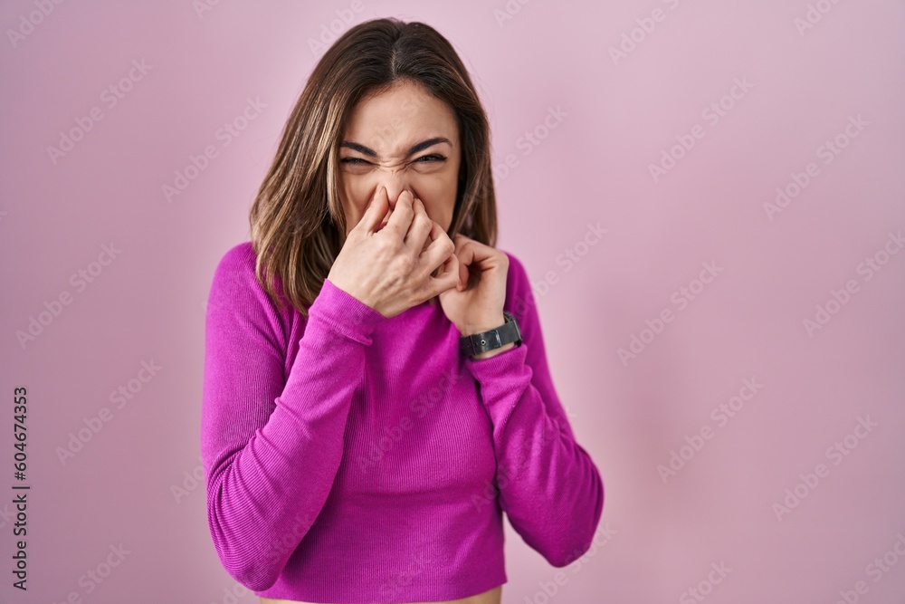 Hispanic woman standing over pink background smelling something stinky and disgusting, intolerable smell, holding breath with fingers on nose. bad smell Hispanic woman standing over pink background smelling something stinky and disgusting, intolerable smell, holding breath with fingers on nose. bad smell