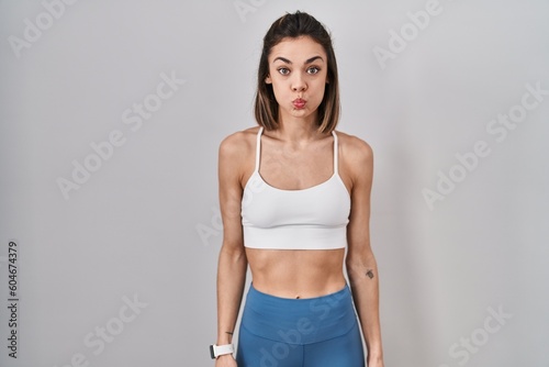 Hispanic woman wearing sportswear over isolated background puffing cheeks with funny face. mouth inflated with air, crazy expression. © Krakenimages.com