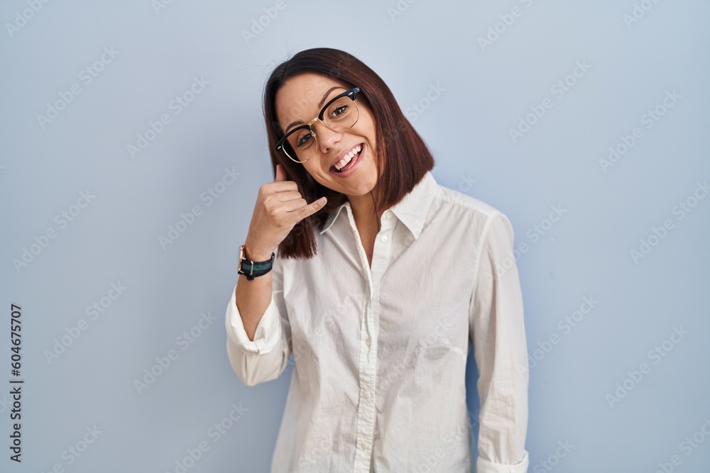 Young hispanic woman standing over white background smiling doing phone gesture with hand and fingers like talking on the telephone. communicating concepts. Young hispanic woman standing over white background smiling doing phone gesture with hand and fingers like talking on the telephone. communicating concepts.