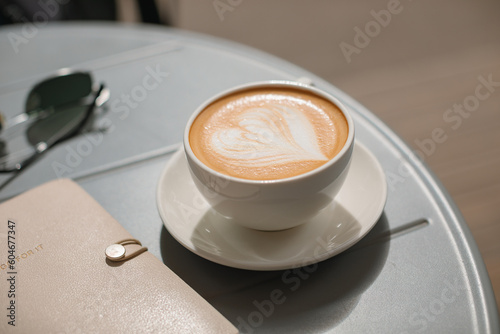 Close-up of a cappuccino on a table next to a diary and a pair of sunglasses photo