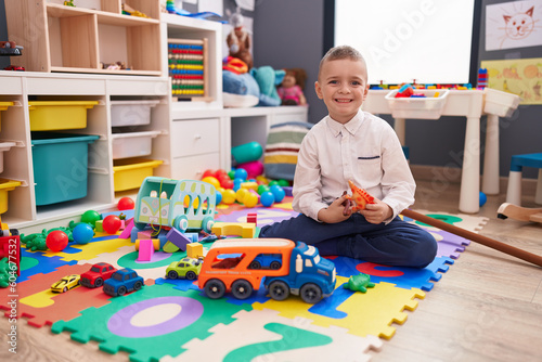 Adorable caucasian boy playing with dinosaur toy sitting on floor at kindergarten