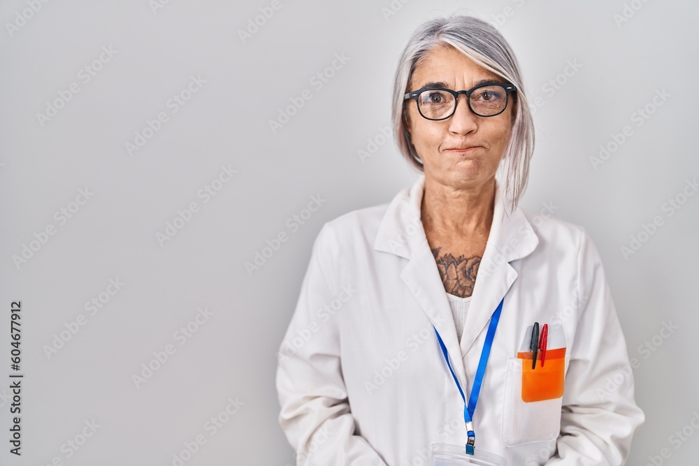 Middle age woman with grey hair wearing scientist robe puffing cheeks with funny face. mouth inflated with air, crazy expression. Middle age woman with grey hair wearing scientist robe puffing cheeks with funny face. mouth inflated with air, crazy expression.