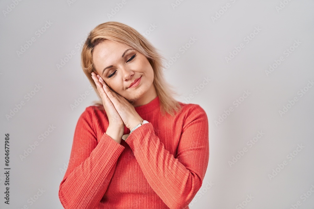 Blonde woman standing over isolated background sleeping tired dreaming and posing with hands together while smiling with closed eyes. Blonde woman standing over isolated background sleeping tired dreaming and posing with hands together while smiling with closed eyes.