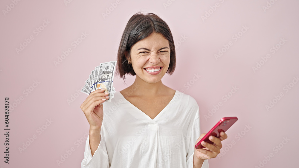 Young beautiful hispanic woman smiling holding dollars and smartphone over isolated pink background Young beautiful hispanic woman smiling holding dollars and smartphone over isolated pink background
