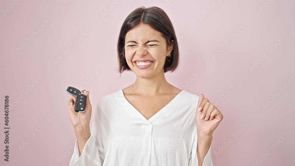 Young beautiful hispanic woman pointing to key of new car with winner expression over isolated pink background Young beautiful hispanic woman pointing to key of new car with winner expression over isolated pink background