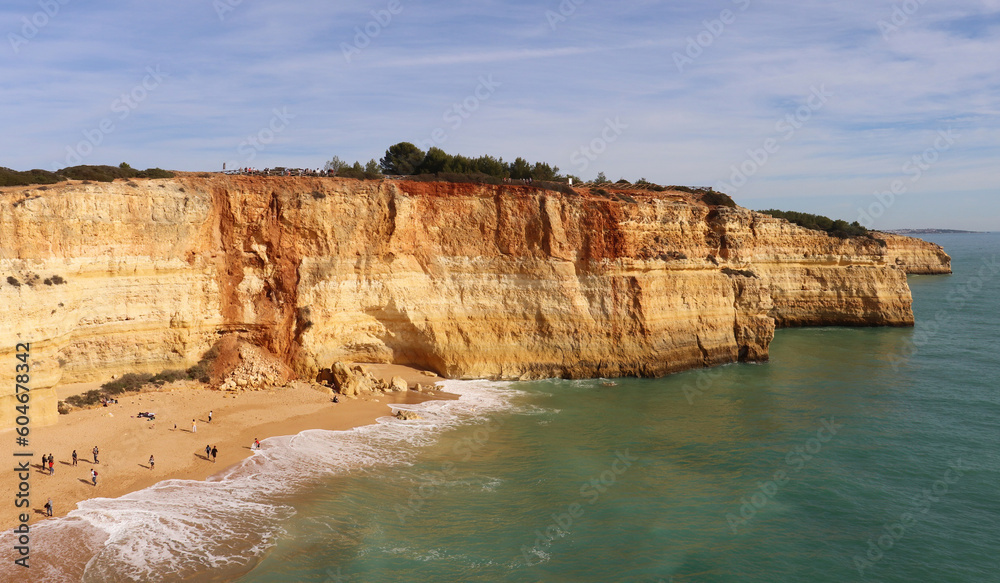 People on a small sady beach surrounded by limestone cliffs next to the Atlantic Ocean on a sunny winter day along the Seven Hanging Valleys Trail in southern Portugal.