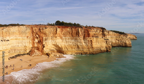 People on a small sady beach surrounded by limestone cliffs next to the Atlantic Ocean on a sunny winter day along the Seven Hanging Valleys Trail in southern Portugal.