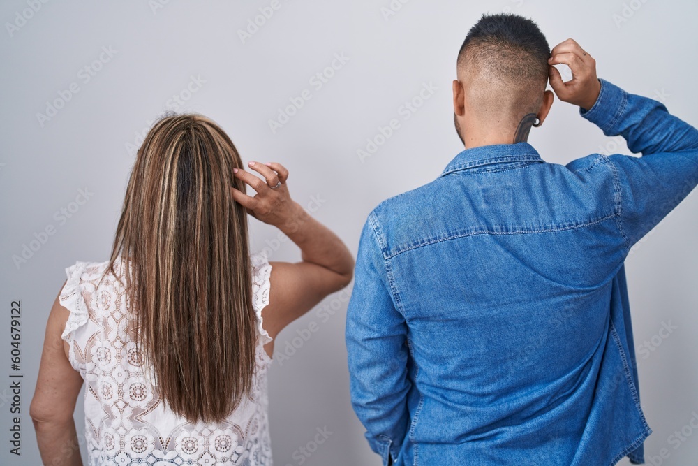 Fototapeta premium Hispanic mother and son standing together backwards thinking about doubt with hand on head