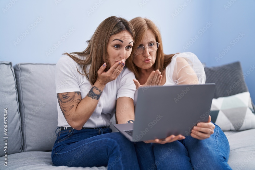 Mother and daughter using laptop sitting on sofa at home
